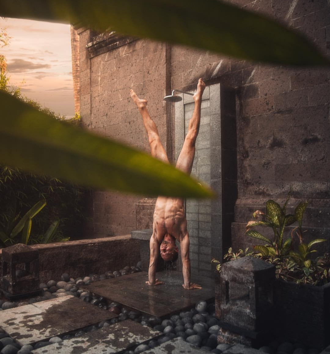 Man doing handstand under a cold shower